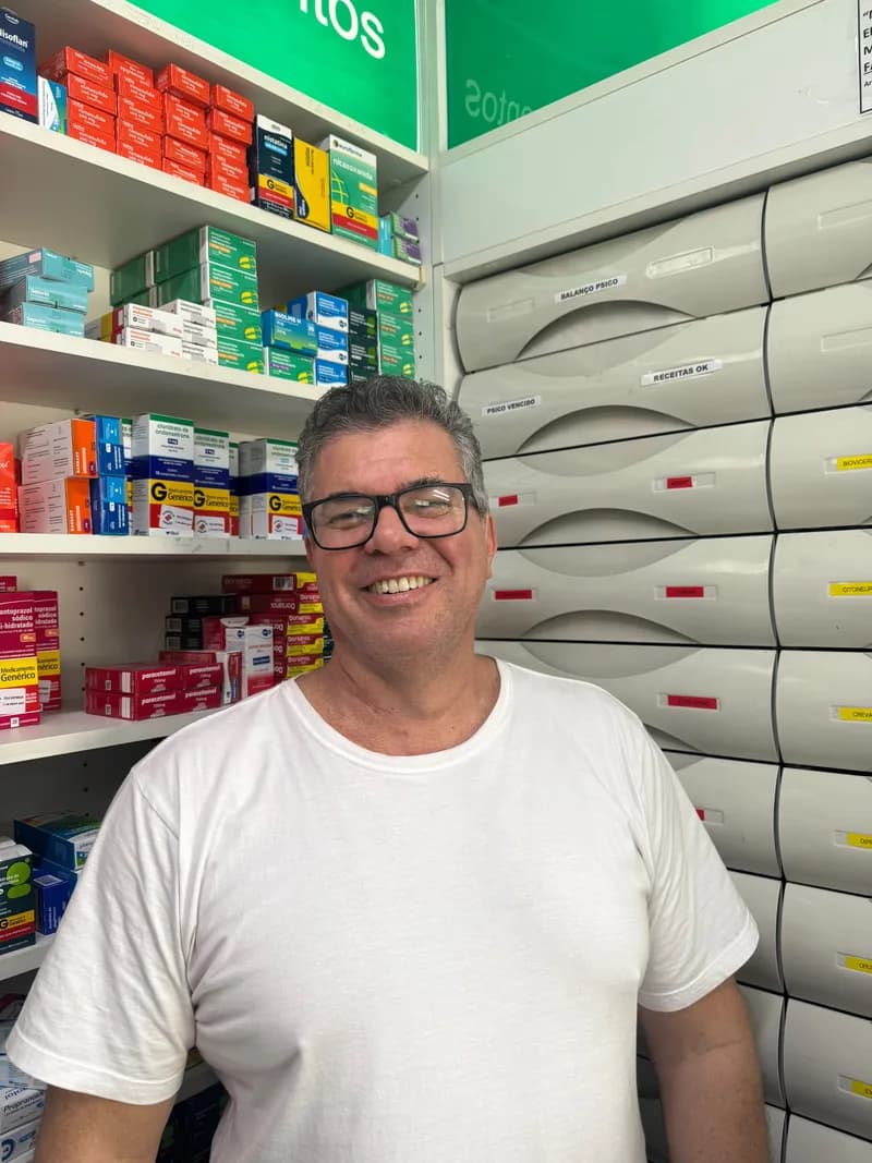 Márcio, farmacêutico da Farmácia Abraão, sorrindo no balcão